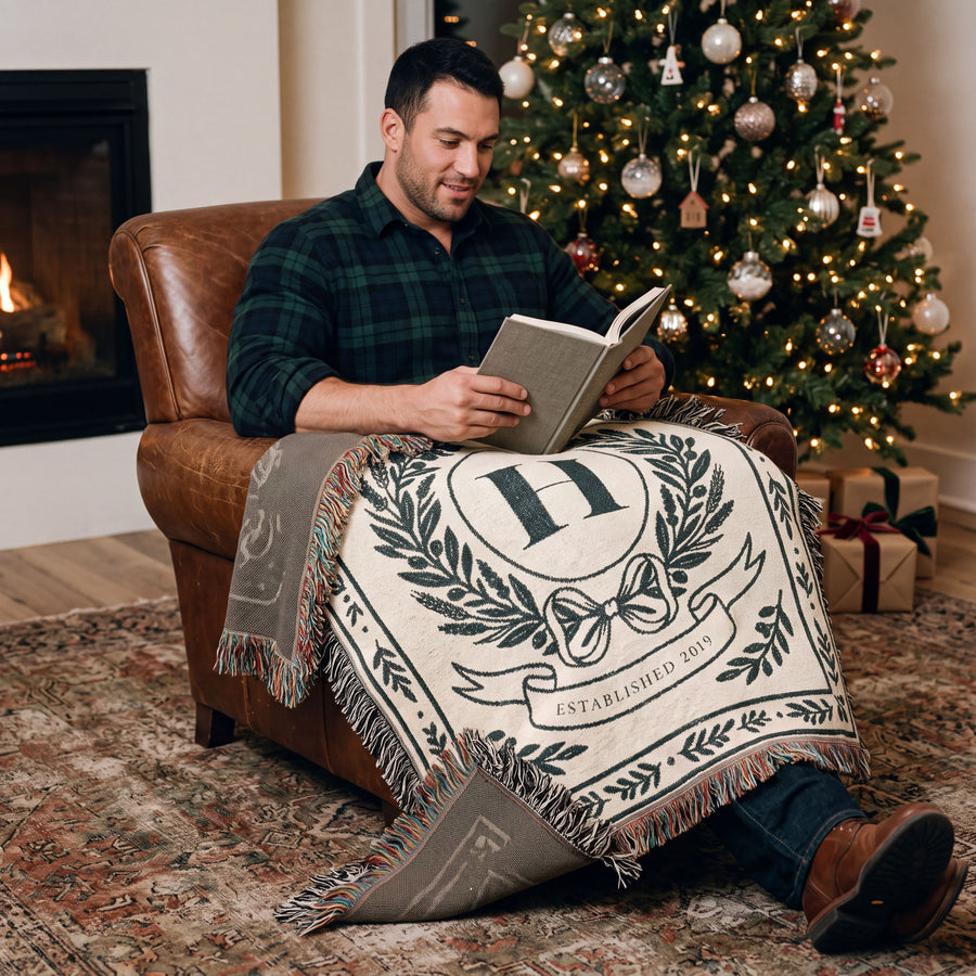 Man reading by a Christmas tree under a personalized family crest woven blanket
