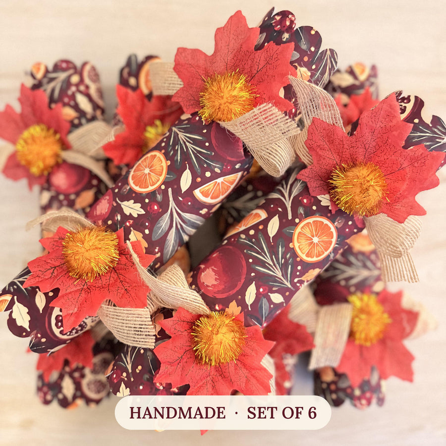 Set of six handmade Mulled and Merry crackers in a citrus and pomegranate print with red maple leaves and gold pom poms