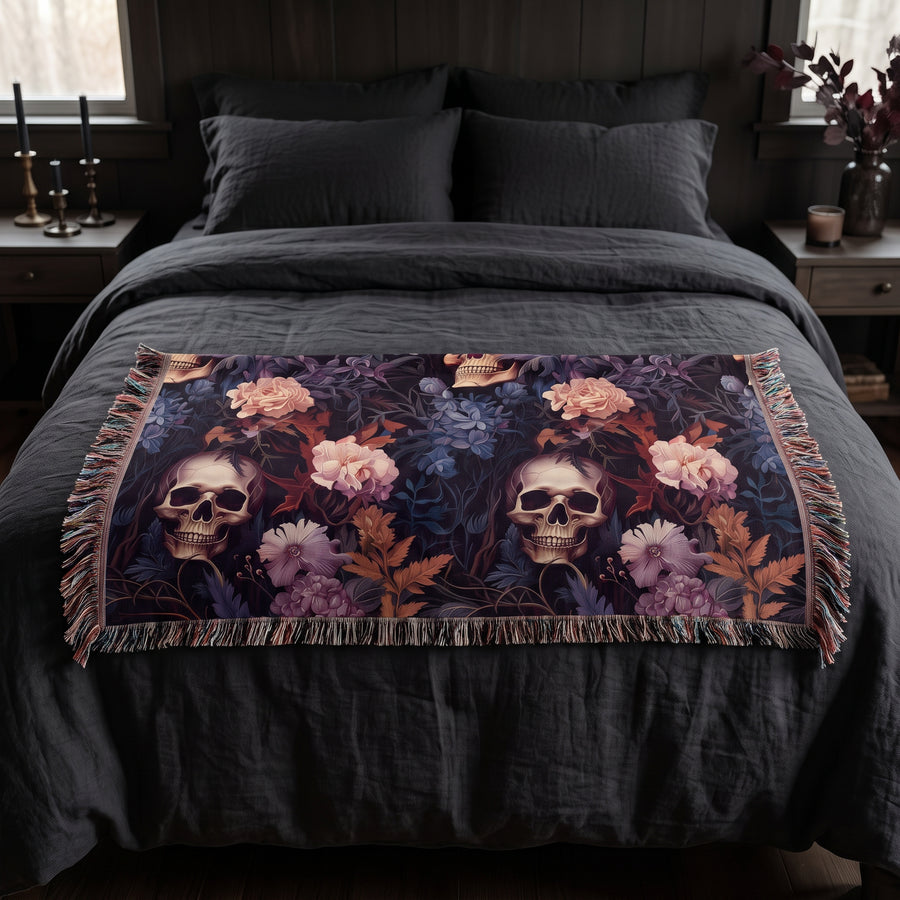 Questionably Cute skull and flowers woven blanket folded across the foot of a queen bed with charcoal linen