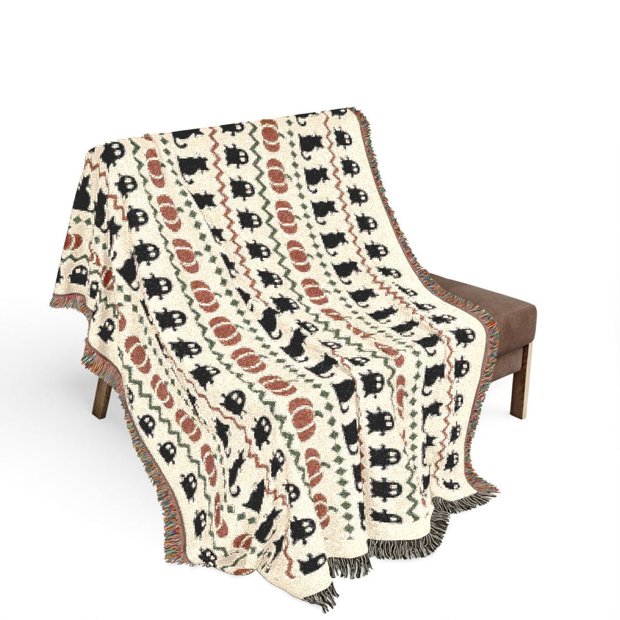 Haunted Heirloom woven blanket draped over a chair, showing the ghost and black cat pattern
