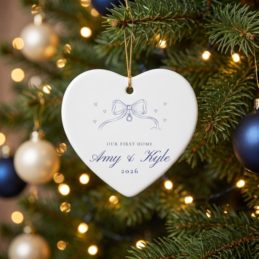 Our First Home personalized ceramic heart ornament with bow, names and year, hanging on a Christmas tree