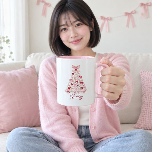 Young woman on a pink and cream couch holding the coquette bow Christmas tree name mug