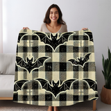 Woman holding the bat plaid Halloween fleece blanket open, black bats on a cream and black tartan check