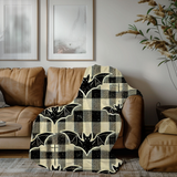Bat plaid Halloween blanket draped over a tan leather sofa in a bright living room