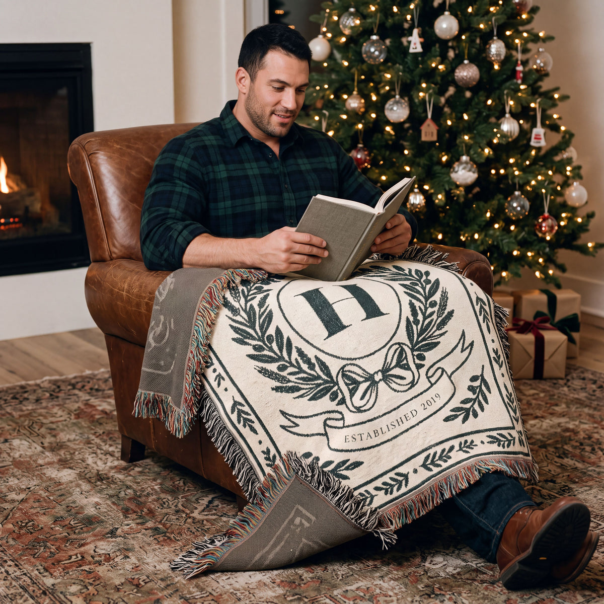 Man reading by a Christmas tree under a personalized family crest woven blanket