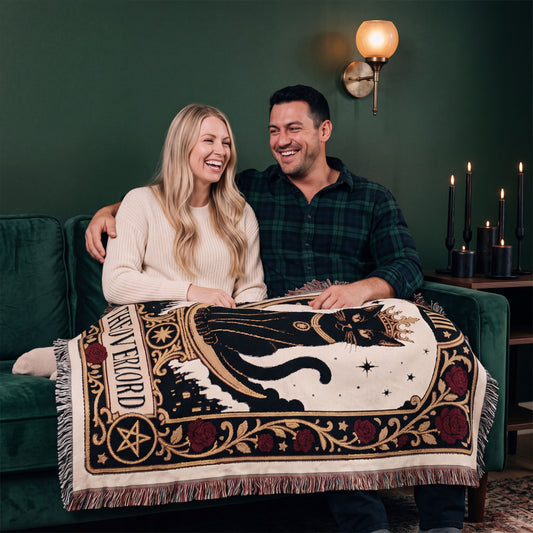 Couple on a green velvet sofa with The Overlord black cat tarot woven blanket across their laps