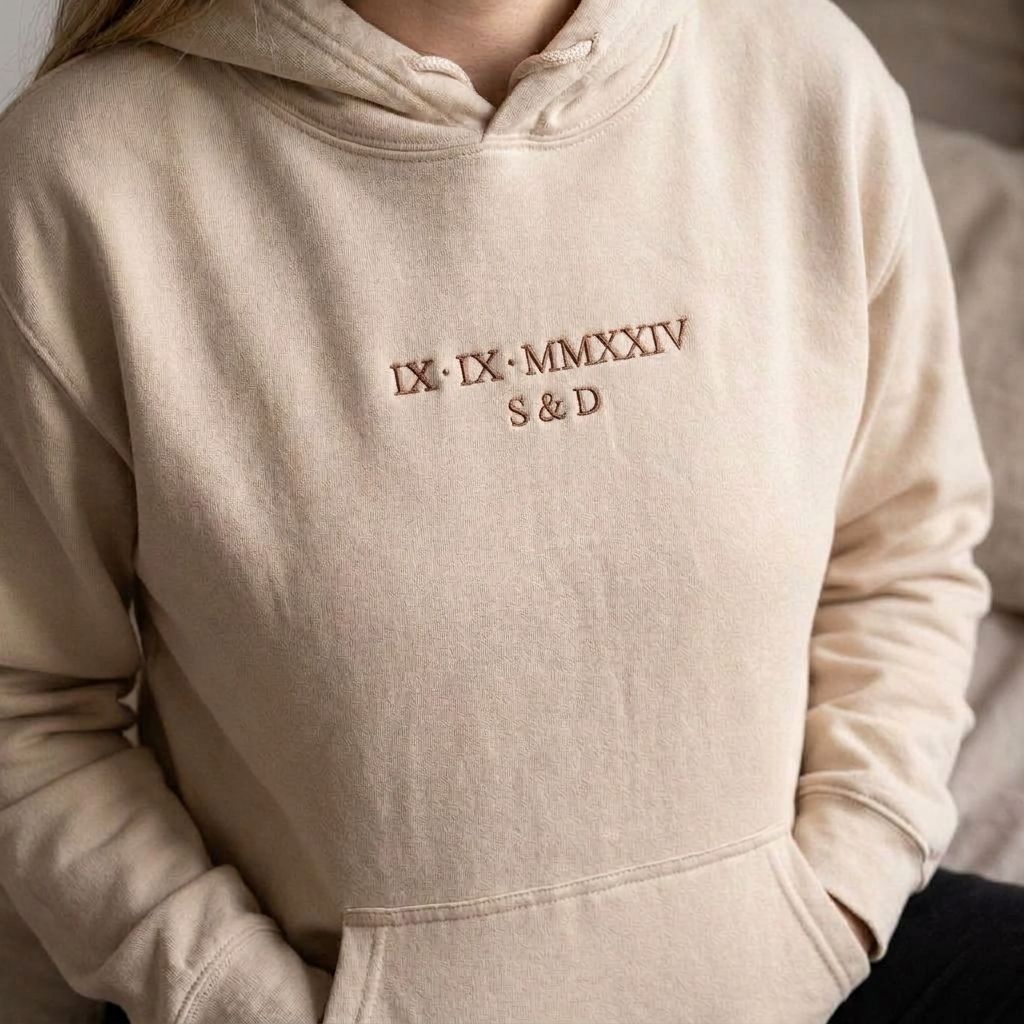 Sand Roman numeral hoodie with IX IX MMXXIV and S & D embroidered in brown thread, about 4 inches wide on the chest