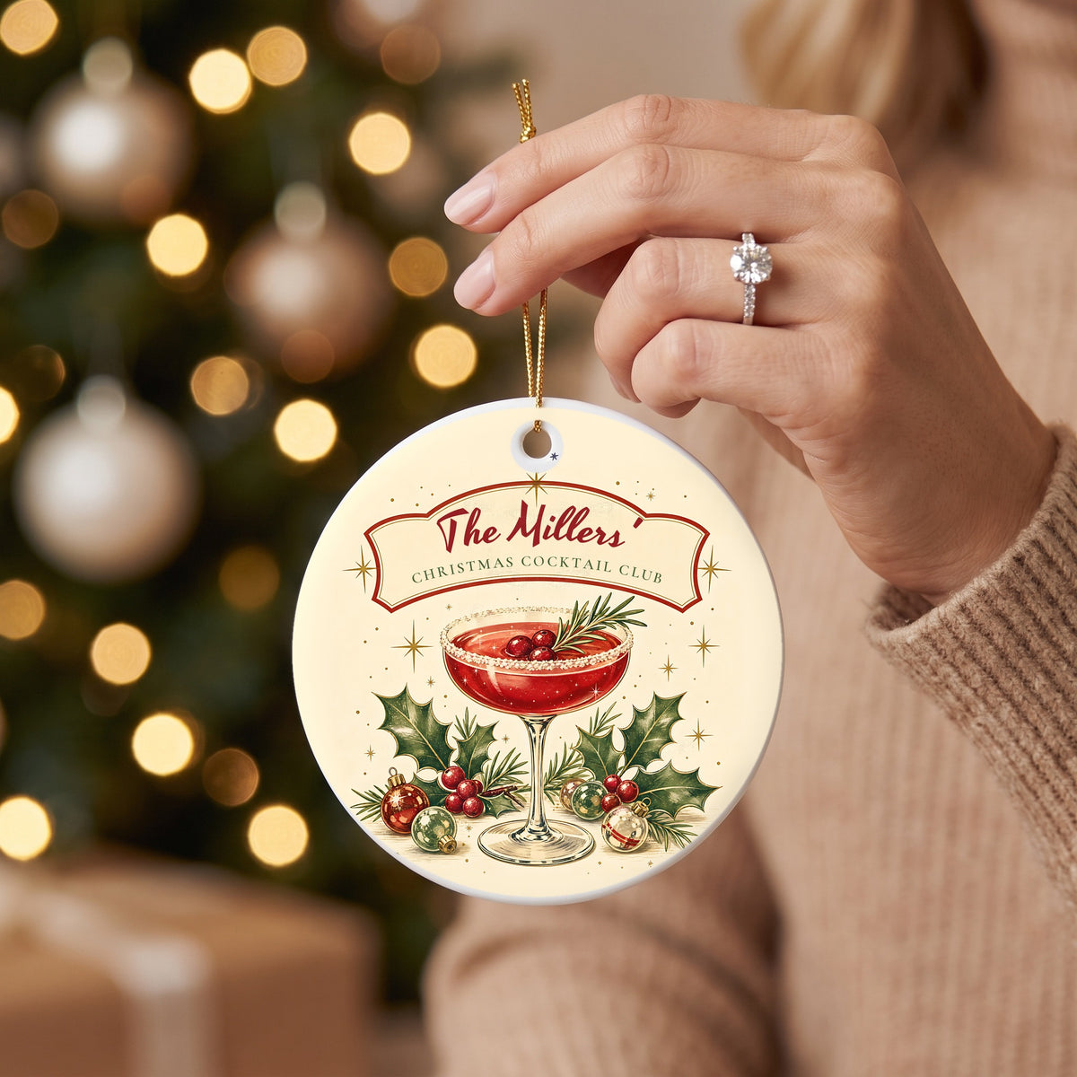 Hand holding the retro cocktail Christmas ornament with a coupe glass, holly and a personalized banner
