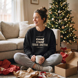 Woman laughing on the couch with a coffee mug in the Black Good Until the 26th sweatshirt by the Christmas tree
