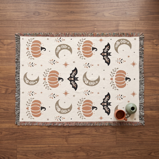 Overhead flatlay of the Subtle Spooky boho Halloween throw on a walnut floor, showing the full scattered pattern of pumpkins, moons and bats with multicoloured fringe