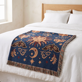 Celestial sun and moon woven blanket folded across the foot of a bed with white linens, showing scale against the mattress