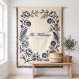 Personalized family name woven blanket, navy botanical on cream cotton, hanging on a white wall