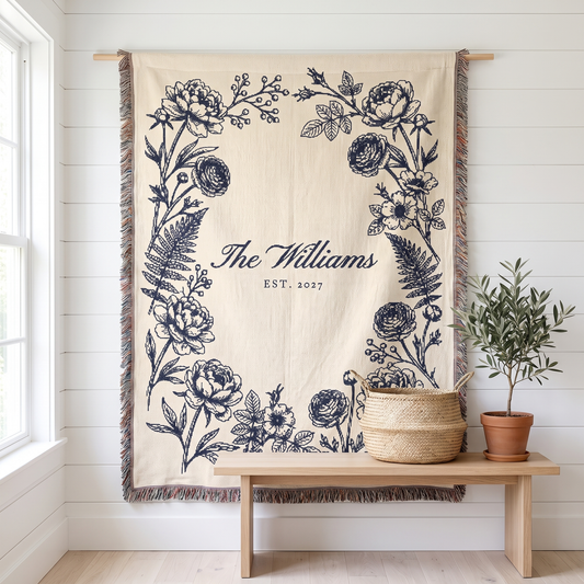 Personalized family name woven blanket, navy botanical on cream cotton, hanging on a white wall