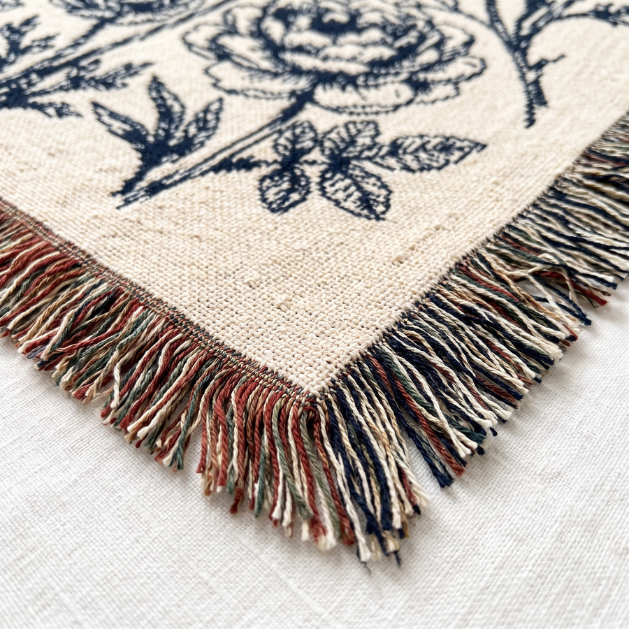 Close up of the woven cotton yarn and fringe on the navy botanical family name blanket
