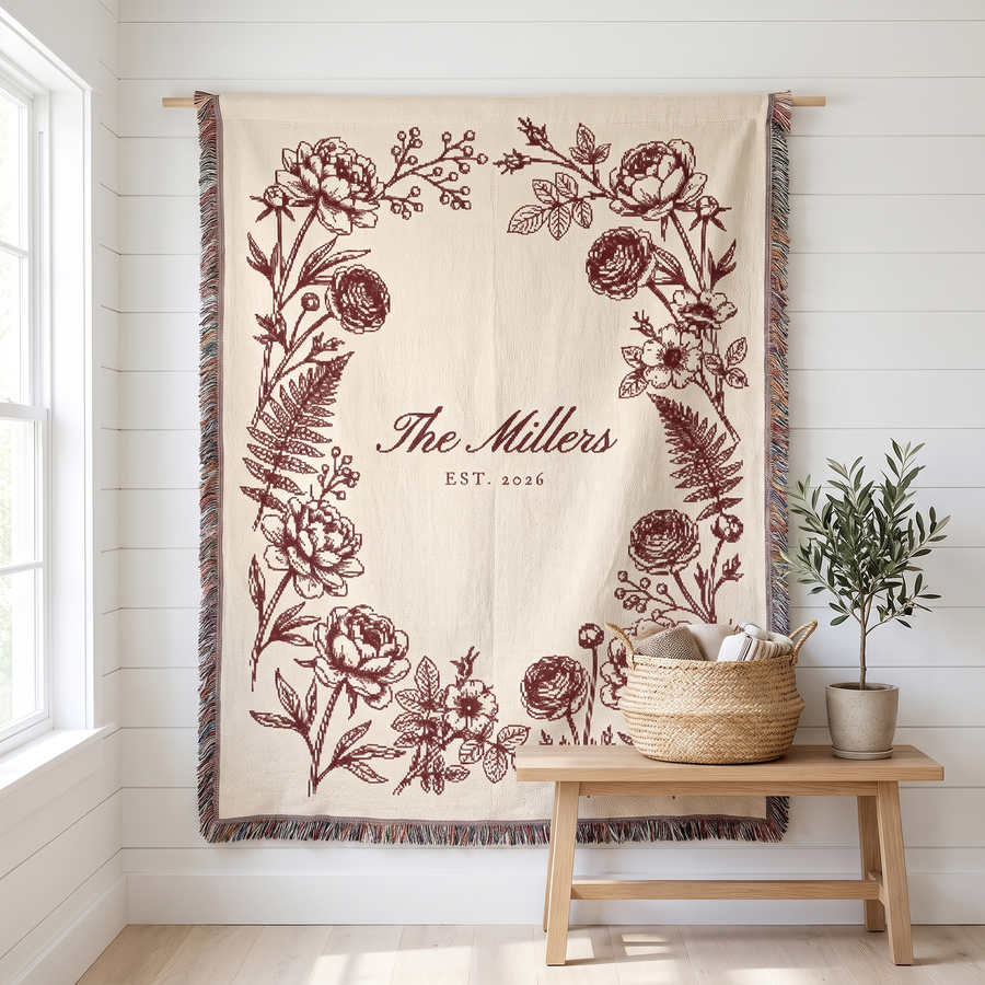 Personalized family name woven blanket, burgundy botanical on cream cotton, hanging on a white wall