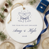 Champagne toast engagement ornament on linen with pine, champagne coupes and an engagement ring box