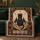 The Overlord black cat tarot woven blanket draped over a green velvet sofa with candles