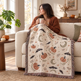 Subtle Spooky Neutral Halloween Woven Blanket over a cream sofa while a woman holds a mug by the window