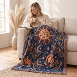 Cosmic Overcommitment Whimsigoth Celestial Woven Blanket over a linen sofa while a woman sips tea with a book