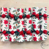 Six red poinsettia Christmas crackers in a row with green ribbon and red pom poms