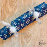 Single blue snowflake cracker on a wooden table, tied at both ends with silver ribbon