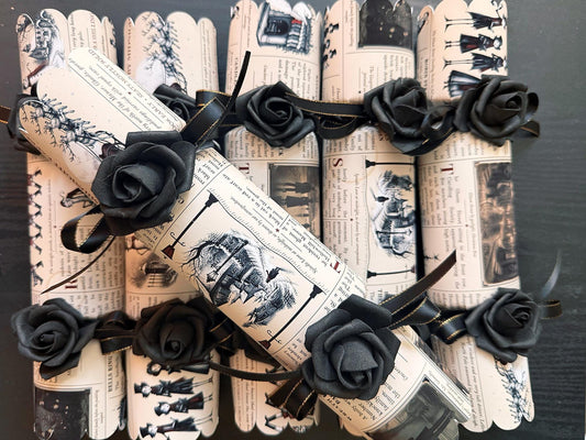 Set of 6 handmade gothic Christmas crackers in cream vintage newspaper print with black ink illustrations, black foam roses and gold-edged black satin ribbon, one cracker laid diagonally on top