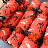 One handmade Halloween cracker on a dark starry background with black satin ribbon and orange pom poms