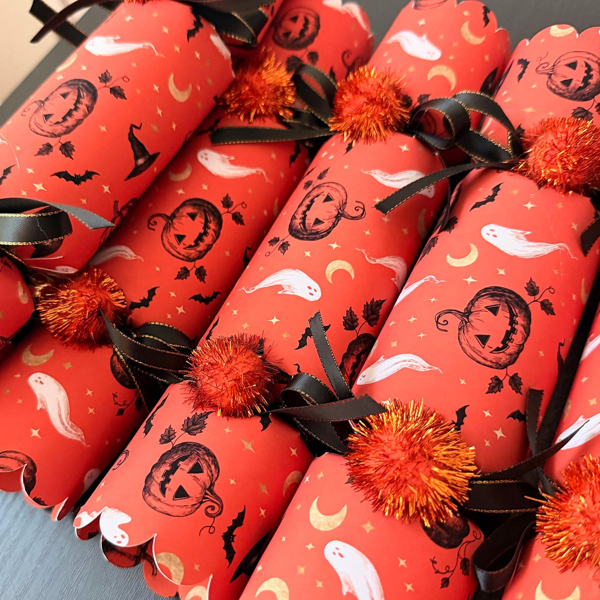 One handmade Halloween cracker on a dark starry background with black satin ribbon and orange pom poms