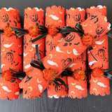 Single Halloween cracker with snap on a dark wood table, tied with black and gold-edged ribbon
