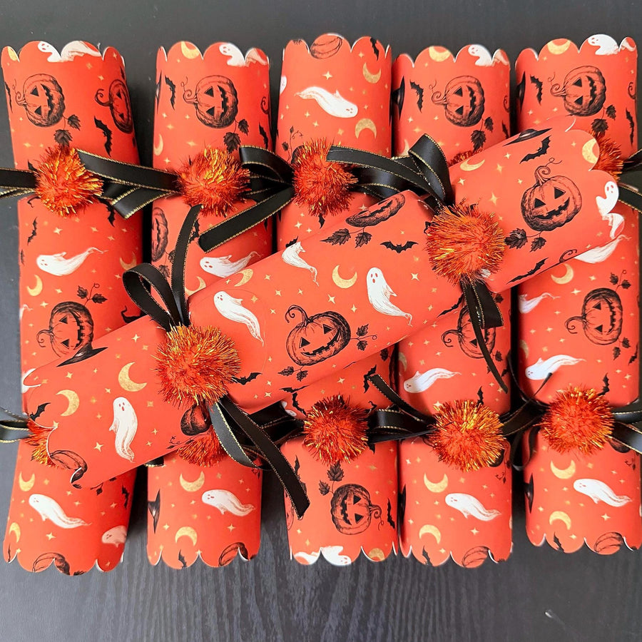Set of 6 handmade Halloween crackers with snaps in a vintage orange print with jack-o'-lanterns, ghosts and gold moons, black ribbon and orange tinsel pom poms