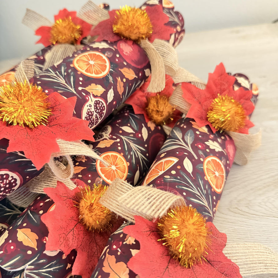 Pile of handmade Thanksgiving and Christmas crackers in deep burgundy with orange slices and gold pom poms