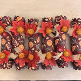 Top-down view of six burgundy crackers with orange slice and pomegranate print, burlap ribbon and red leaves