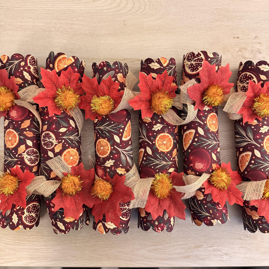 Top-down view of six burgundy crackers with orange slice and pomegranate print, burlap ribbon and red leaves