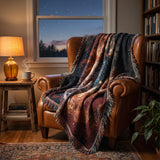 James Webb Tarantula Nebula woven blanket draped over a cognac leather armchair in a cozy reading nook at dusk