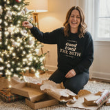 Woman trimming the Christmas tree in the Black Good Until the 26th sweatshirt with twinkling lights