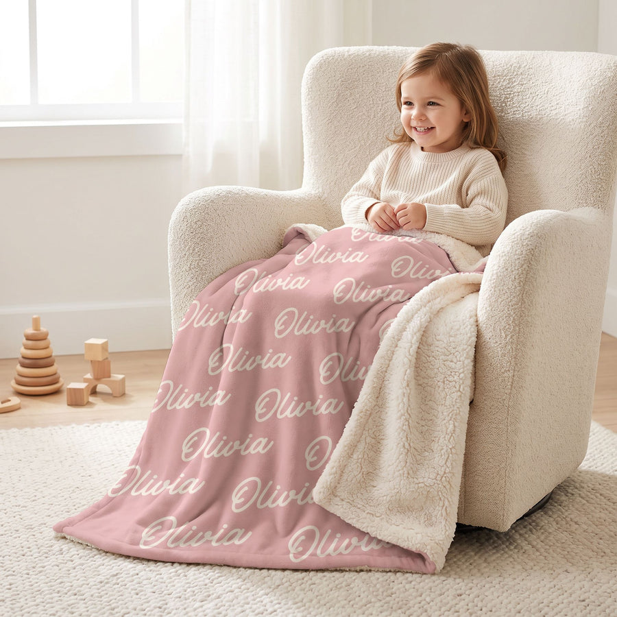 Toddler girl cozy in a cream armchair under a custom name blanket with Olivia printed all over