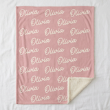 Flat lay of the personalized name throw blanket on a white bed showing the full repeating name pattern and sherpa corner