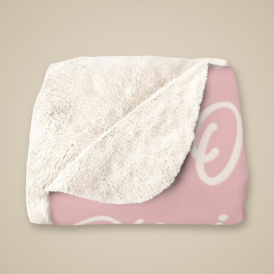 Name blanket folded with the soft cream sherpa reverse turned back over the pink printed fleece front