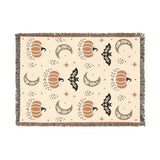 Subtle Spooky neutral Halloween woven blanket laid flat, cream weave with orange pumpkins, tan moons and black bats, multicolor fringe